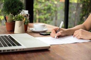 A person filling out a form with a laptop in front of them