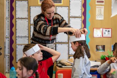A teacher helps children make paper crowns.
