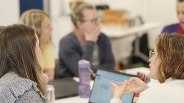 A group of teachers sit around a table, discussing.
